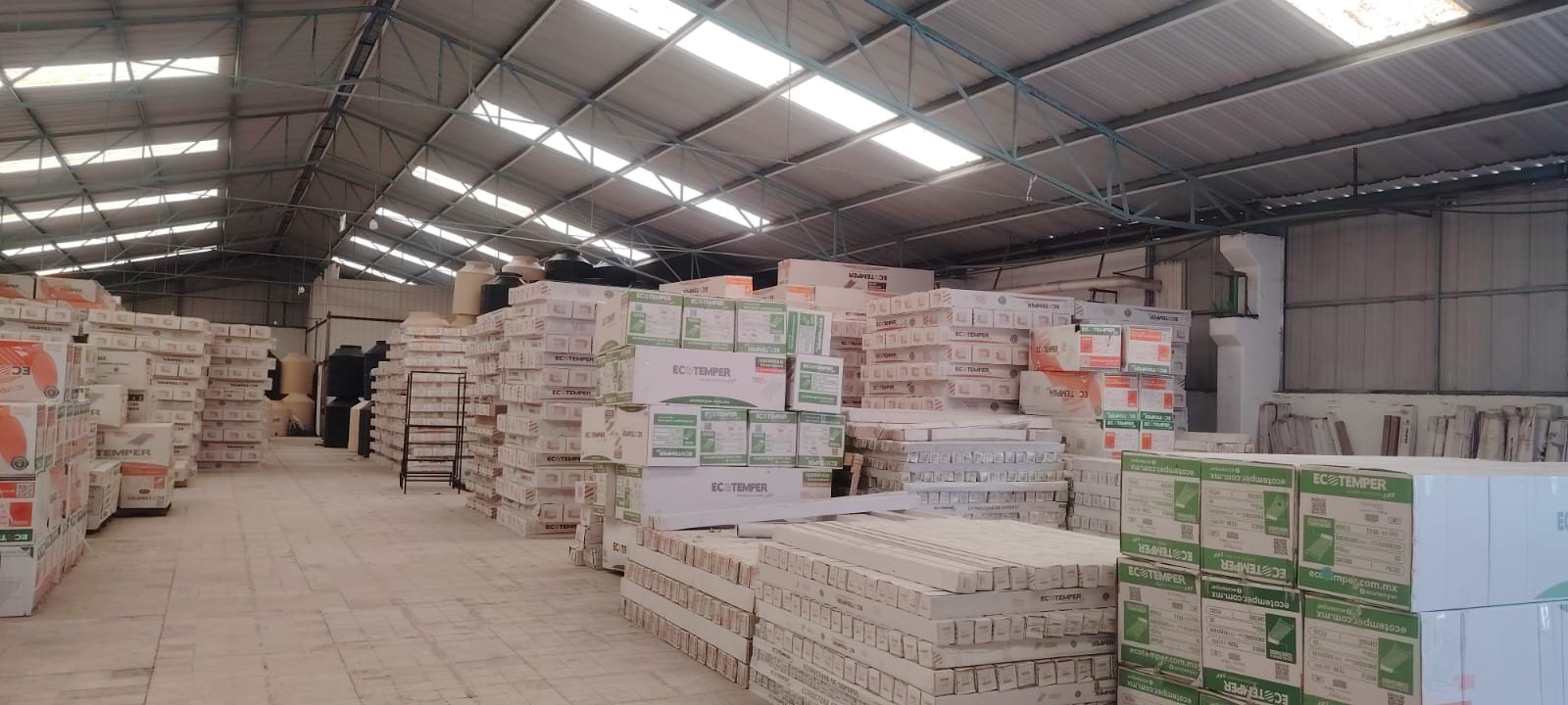 Nave industrial real de SOLCAE en Ecatepec, pasillo alto con inventario apilado de calentadores solares y tinacos Ecotemper.